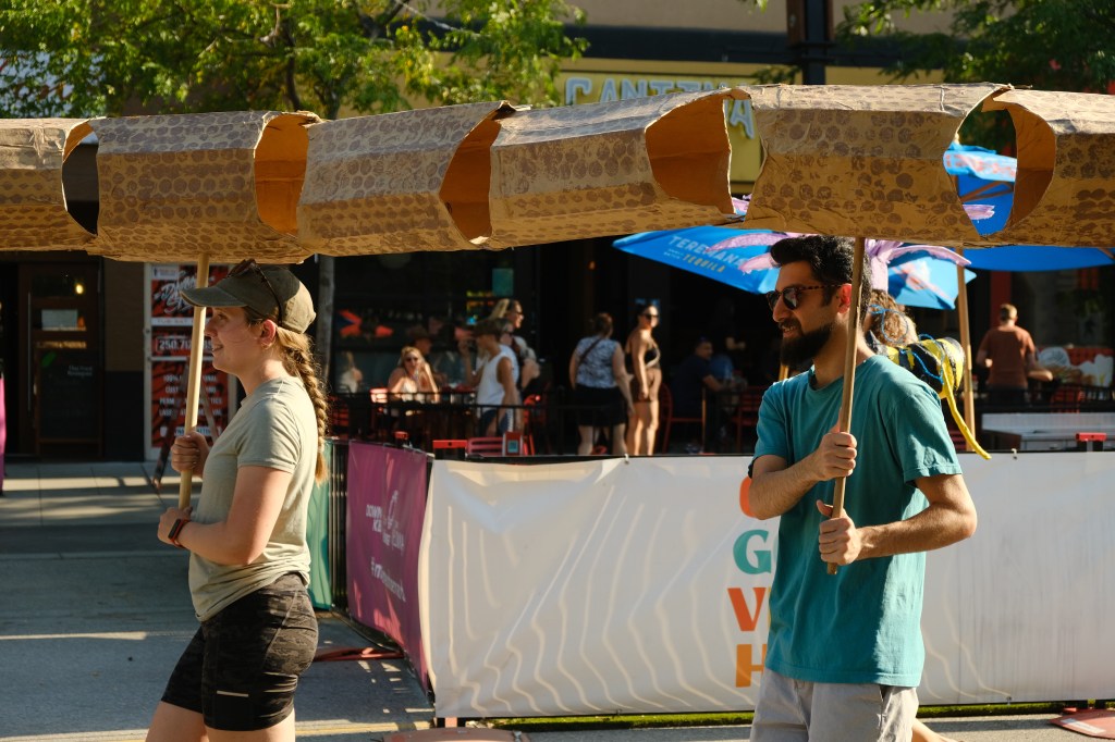 Two peple hold up consecutive parts of a snake puppet.